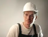 Content male builder in workwear and hardhat smiling on gray background in studio and looking at camera