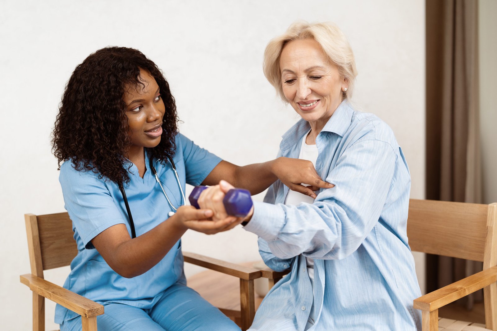 nurse assisting senior woman with physical therapy exercise using dumbbell